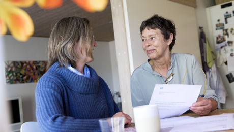 To kvinder taler sammen ved et bord og kigger i papirer