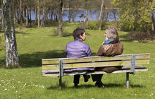 To kvinder sidder med ryggen til på en bænk i en park og taler sammen